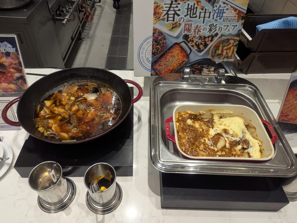 春の地中海リゾートフェアのパエリア風鍋とオムレツグラタンがSTAUB鍋に入った状態、奥にフェアPOP