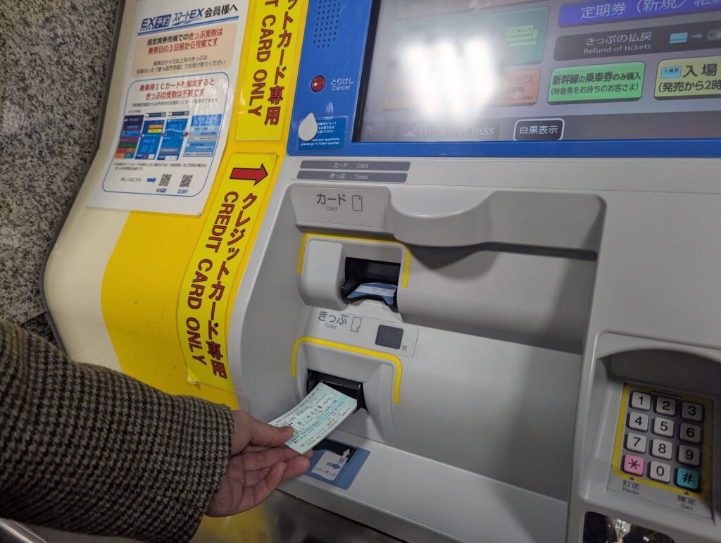 券売機から出てきたきっぷを受け取る場面