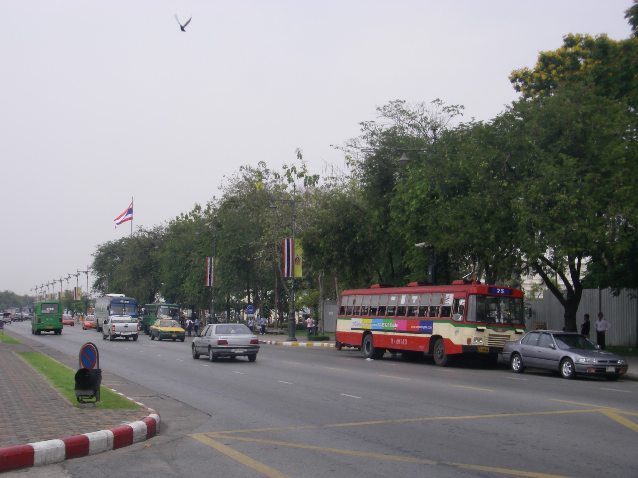 タイの国旗が並ぶ並木道と、赤とクリーム色の路線バス