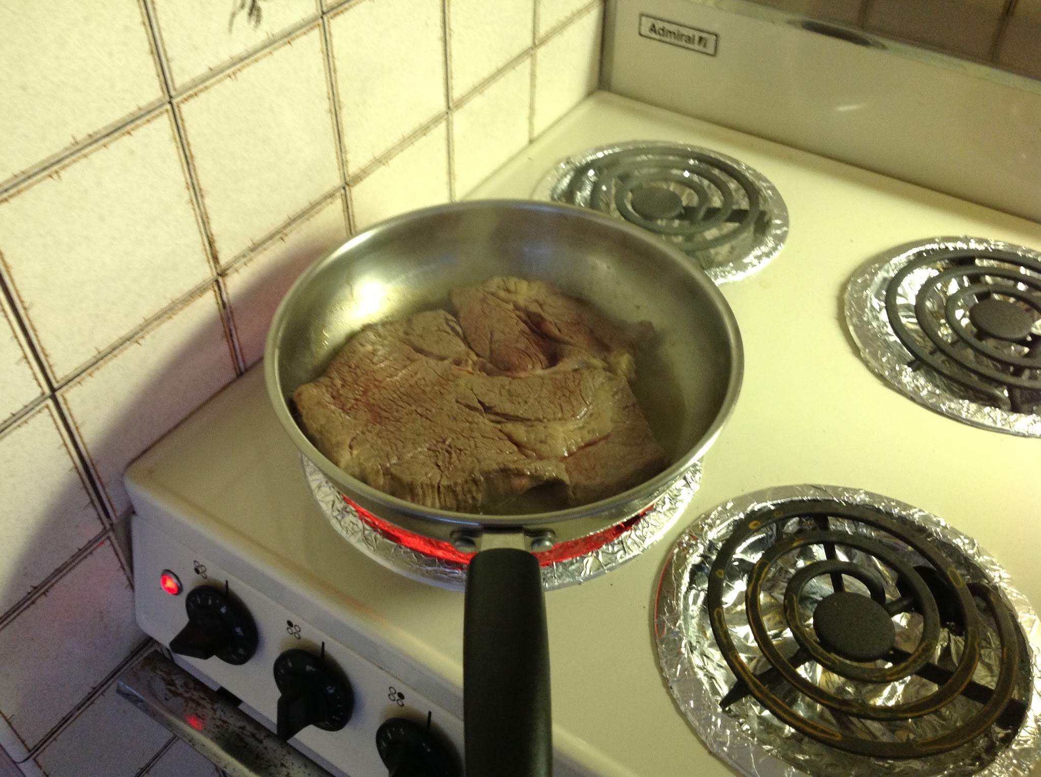電気コンロでフライパンに入れた肉を焼いている様子
